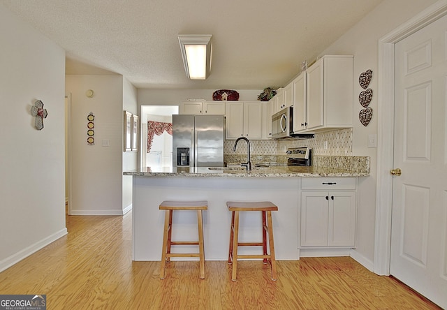 kitchen with light wood finished floors, a peninsula, a sink, stainless steel appliances, and backsplash