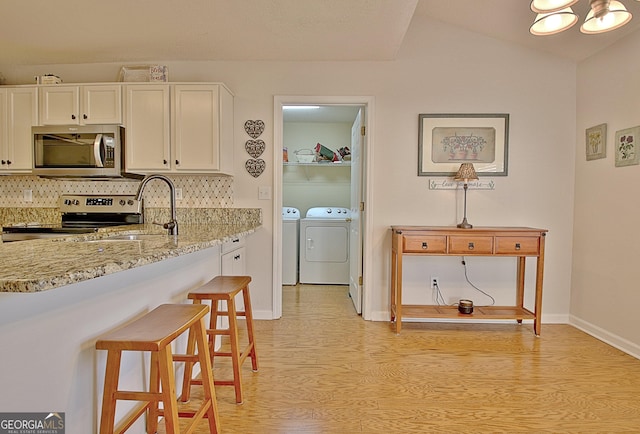 kitchen featuring light wood finished floors, tasteful backsplash, washer and clothes dryer, appliances with stainless steel finishes, and white cabinetry