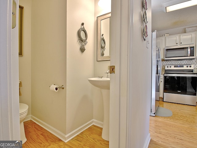 half bath featuring baseboards, backsplash, toilet, and wood finished floors