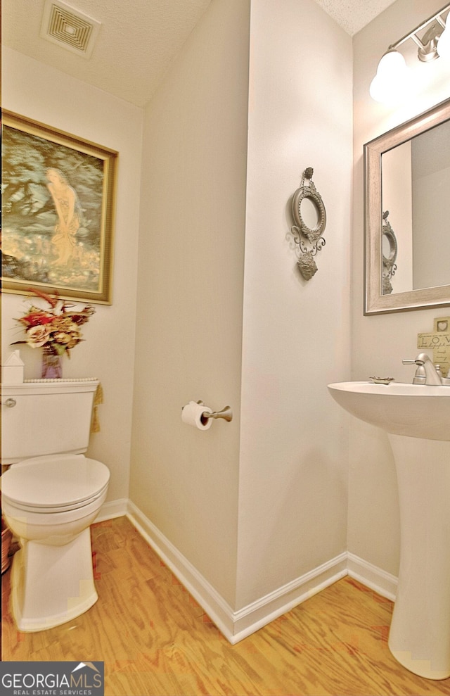 half bathroom featuring toilet, wood finished floors, visible vents, and baseboards