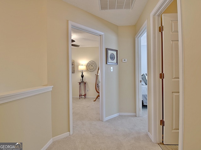 hallway with baseboards, visible vents, and light colored carpet