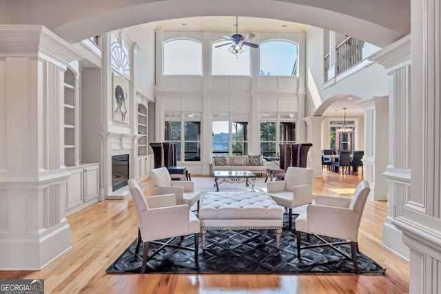 living room featuring built in features, arched walkways, a glass covered fireplace, a decorative wall, and a wealth of natural light