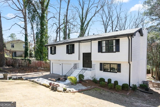 bi-level home with a garage, driveway, a chimney, fence, and brick siding