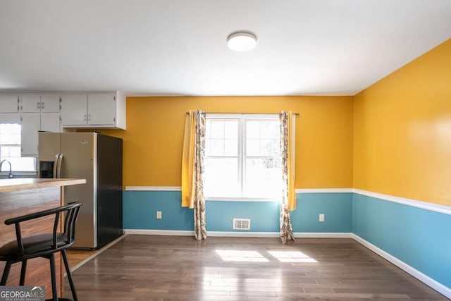 interior space with white cabinetry, visible vents, baseboards, stainless steel refrigerator with ice dispenser, and dark wood finished floors