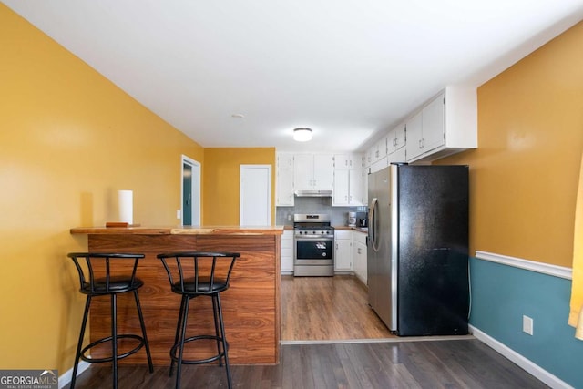 kitchen with under cabinet range hood, stainless steel appliances, a peninsula, white cabinetry, and backsplash