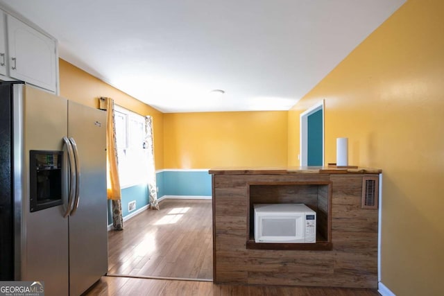 kitchen with baseboards, white microwave, wood finished floors, white cabinetry, and stainless steel refrigerator with ice dispenser