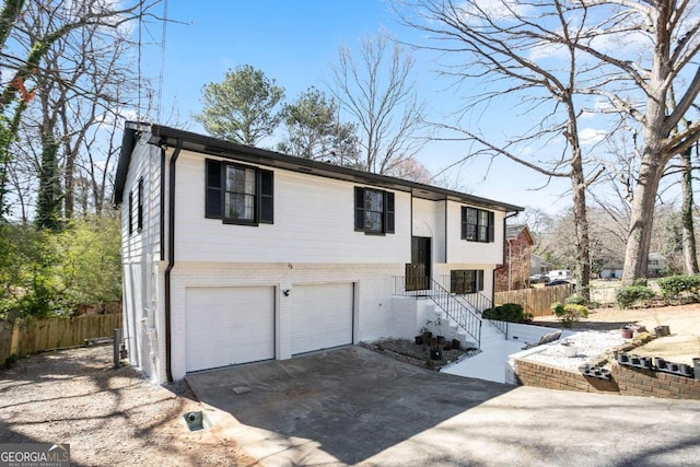 bi-level home featuring brick siding, driveway, an attached garage, and fence