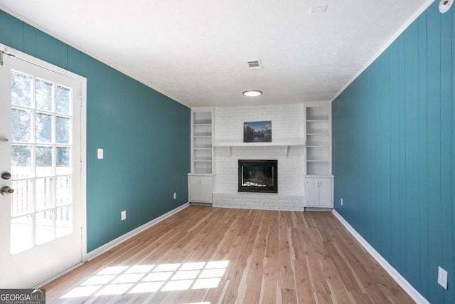 unfurnished living room featuring built in features, visible vents, a brick fireplace, wood finished floors, and baseboards