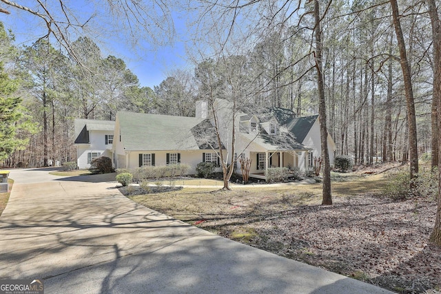 cape cod house featuring concrete driveway and a chimney