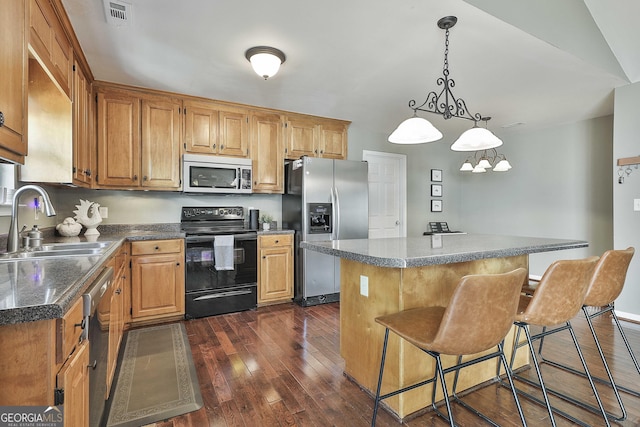 kitchen with a kitchen island, dark wood finished floors, appliances with stainless steel finishes, a kitchen breakfast bar, and a sink