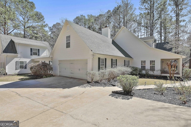 view of side of property with concrete driveway, a garage, and a chimney