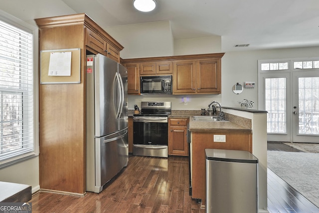 kitchen featuring dark wood-type flooring, a sink, appliances with stainless steel finishes, a peninsula, and brown cabinetry