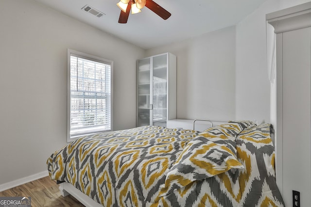 bedroom with a ceiling fan, wood finished floors, visible vents, and baseboards