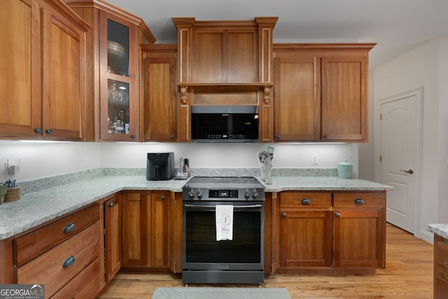 kitchen with light stone counters, electric range, brown cabinetry, light wood-type flooring, and black microwave