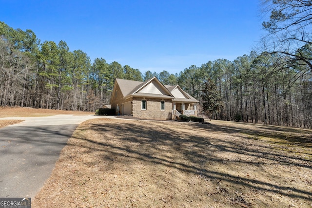 view of front of home with aphalt driveway, a porch, an attached garage, a front yard, and a view of trees