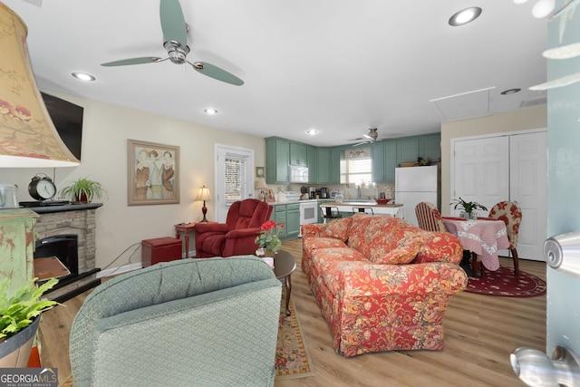 living room featuring light wood-type flooring, a fireplace, a ceiling fan, and recessed lighting