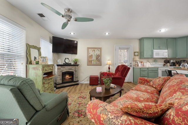 living room with light wood finished floors, visible vents, ceiling fan, a fireplace, and recessed lighting