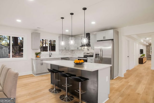 kitchen with wall chimney range hood, appliances with stainless steel finishes, light countertops, and a sink