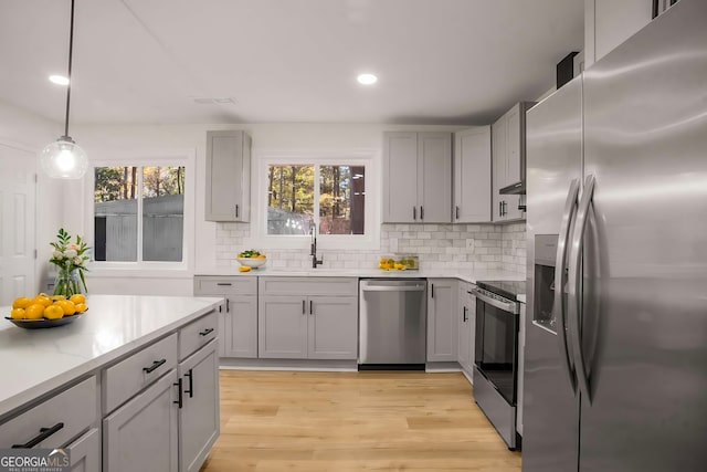 kitchen with stainless steel appliances, a sink, light wood-style flooring, and gray cabinetry