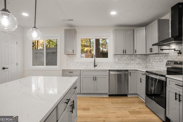 kitchen with stainless steel appliances, gray cabinetry, light wood-style floors, a sink, and wall chimney range hood