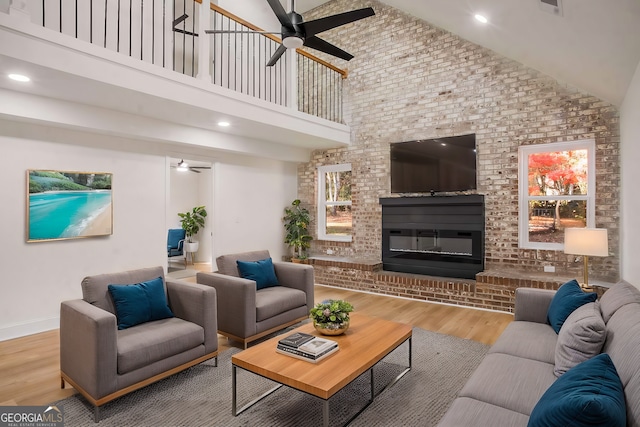 living area with baseboards, ceiling fan, wood finished floors, a fireplace, and high vaulted ceiling