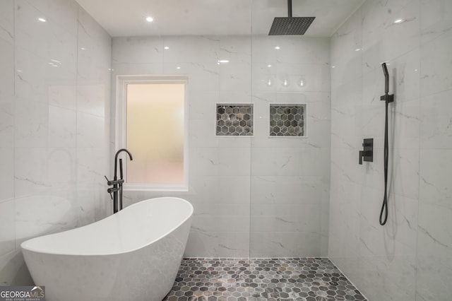 full bathroom with a soaking tub, a marble finish shower, and tile walls