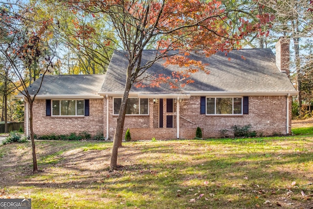 view of front facade with a shingled roof, brick siding, a chimney, and a front lawn