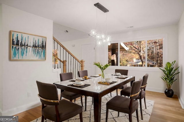 dining space featuring baseboards, light wood-type flooring, visible vents, and a notable chandelier