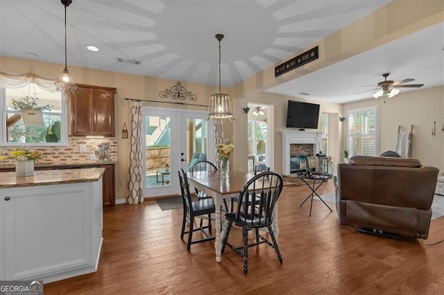 dining room with a ceiling fan, dark wood finished floors, french doors, and a fireplace