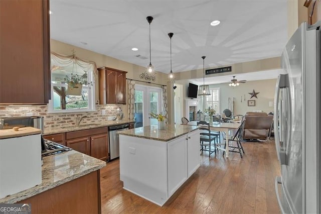 kitchen with open floor plan, a center island, light stone countertops, stainless steel appliances, and a sink