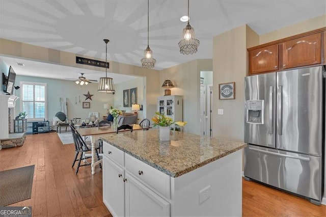 kitchen featuring light stone counters, a kitchen island, open floor plan, stainless steel refrigerator with ice dispenser, and light wood finished floors