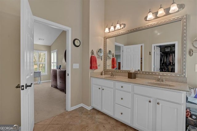 full bathroom featuring double vanity, baseboards, a walk in closet, and a sink