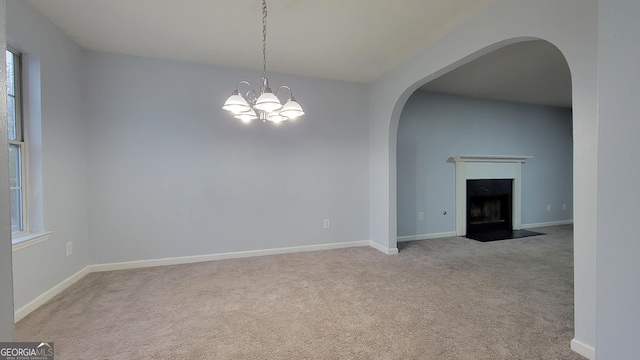 spare room with arched walkways, a notable chandelier, carpet floors, a fireplace with flush hearth, and baseboards