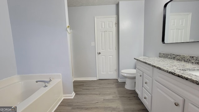 bathroom featuring toilet, wood finished floors, a garden tub, a textured ceiling, and vanity