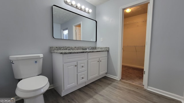 bathroom with baseboards, toilet, wood finished floors, a walk in closet, and vanity