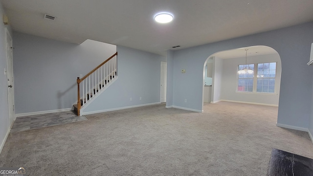 unfurnished living room featuring arched walkways, carpet, visible vents, stairway, and baseboards