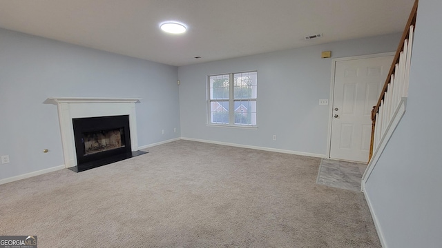 unfurnished living room featuring visible vents, a fireplace with flush hearth, carpet flooring, baseboards, and stairs