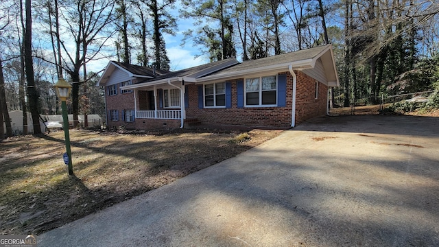 view of front of house featuring concrete driveway, brick siding, a porch, and fence