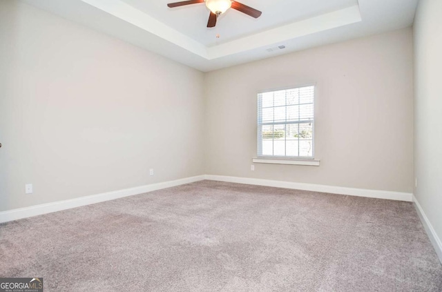 empty room with carpet flooring, a raised ceiling, visible vents, and baseboards