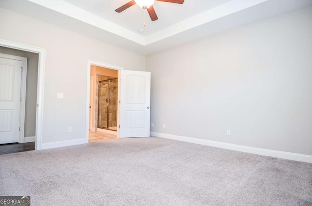 unfurnished bedroom featuring light carpet, baseboards, a raised ceiling, a ceiling fan, and connected bathroom