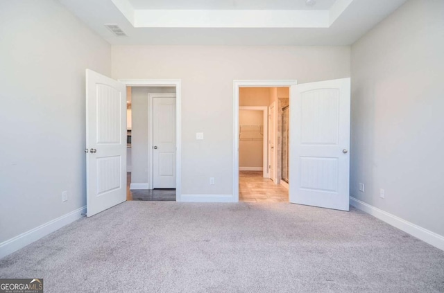 unfurnished bedroom with a raised ceiling, carpet flooring, a spacious closet, and baseboards