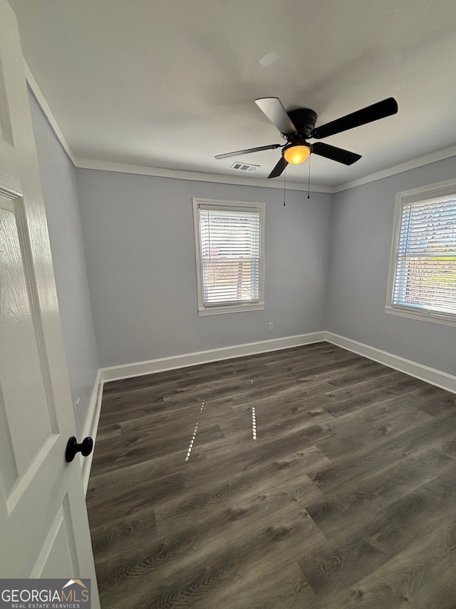 empty room with crown molding, visible vents, and dark wood finished floors