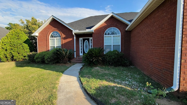 exterior space featuring a shingled roof, a front yard, and brick siding