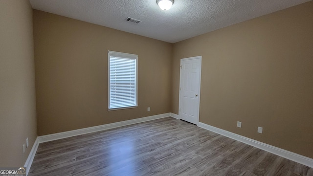 empty room with a textured ceiling, wood finished floors, visible vents, and baseboards