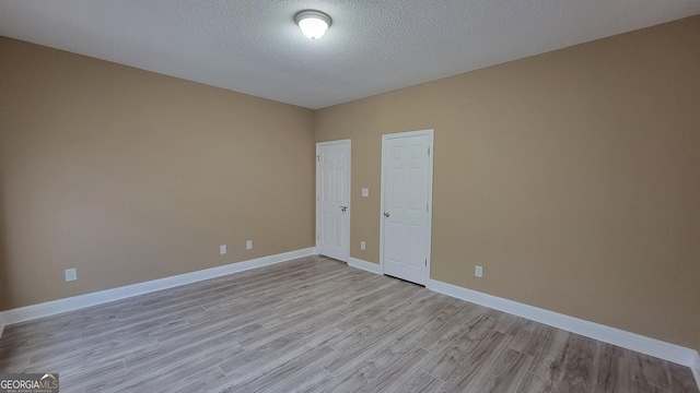 spare room with light wood-style floors, a textured ceiling, and baseboards