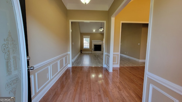 corridor with a wainscoted wall, light wood finished floors, and a decorative wall