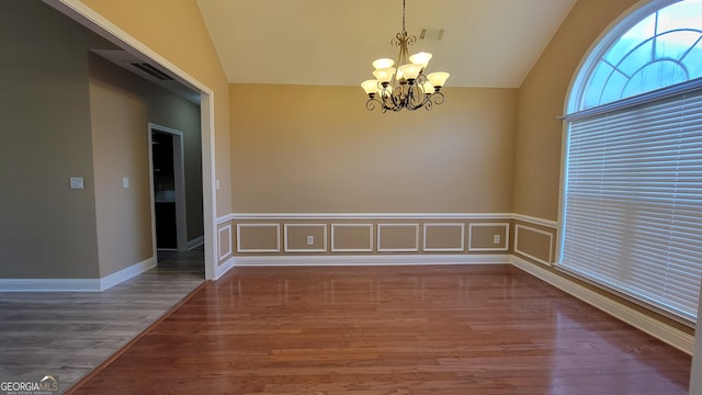 unfurnished room featuring lofted ceiling, visible vents, a decorative wall, wood finished floors, and a chandelier