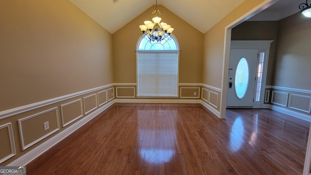 foyer entrance featuring lofted ceiling, a decorative wall, a wainscoted wall, a notable chandelier, and dark wood-type flooring