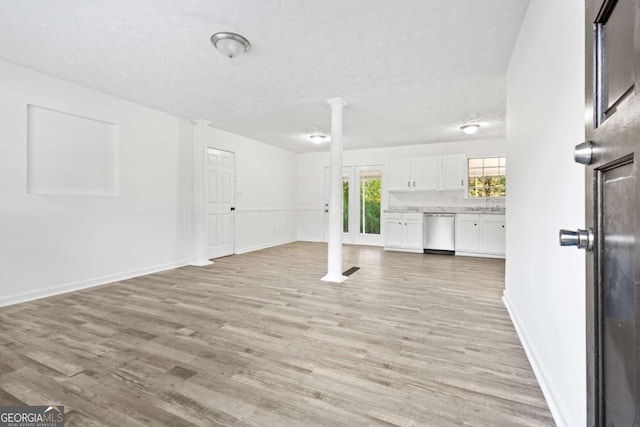 unfurnished living room featuring baseboards, light wood-style flooring, a sink, a textured ceiling, and ornate columns