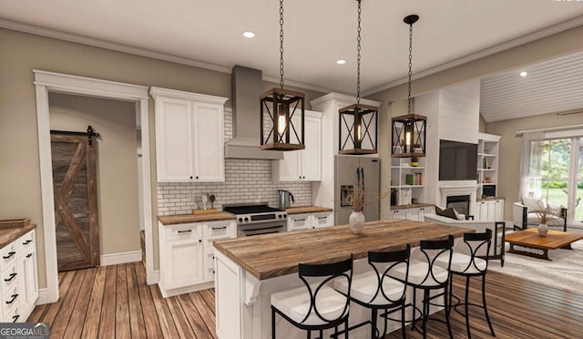 kitchen featuring a barn door, a breakfast bar area, stainless steel appliances, wooden counters, and wall chimney exhaust hood